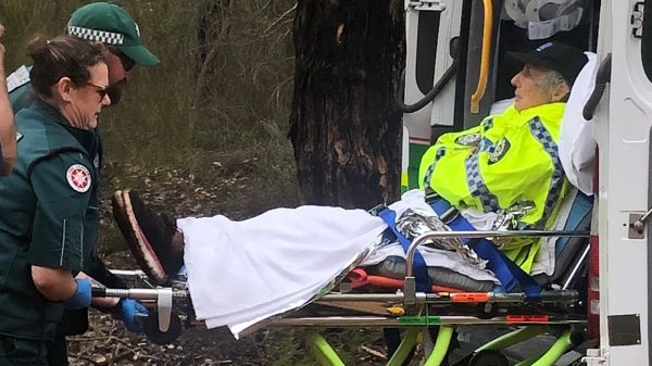 A woman in a hi-vis WA Police jacket lies on a gurney as two St John Ambulance personnel load it into the back of an ambulance.