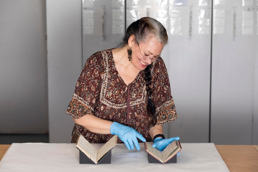 A woman with blue plastic gloves on looks through the pages of an old notebook