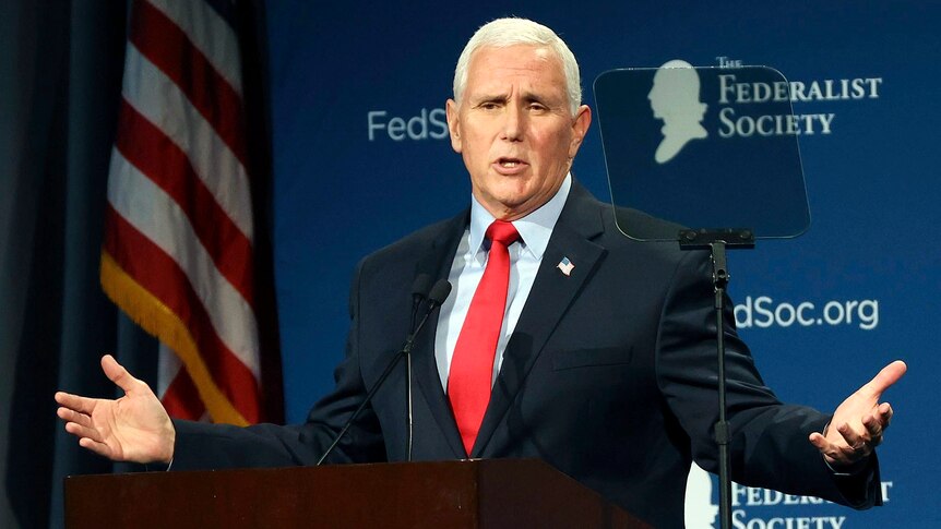 Former Vice President Mike Pence holds his arms out wide in a gesture as he speaks from a podium.