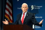 Former Vice President Mike Pence holds his arms out wide in a gesture as he speaks from a podium.