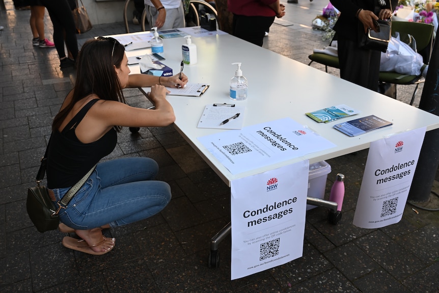 A woman squats down to write on a clipboard on a fold-out table outdoors