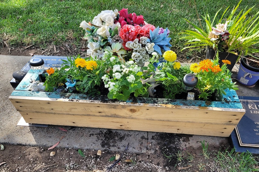 A raised wooden box filled with flowers and trinkets.