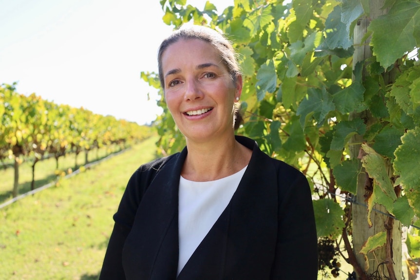 A woman stands in a vineyard. She is smiling at the camera.