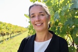 A woman stands in a vineyard. She is smiling at the camera.