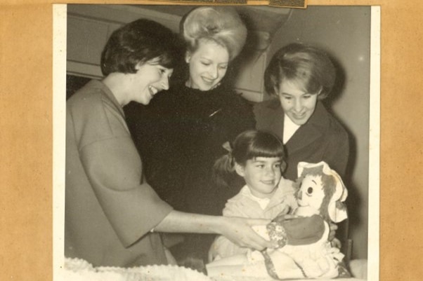 A black and white photos of Dale as a young child. Dale is holding a rag doll and three women are smiling at her.