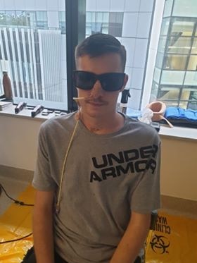 Young man wearing sunglasses sitting up and still with a tube attached to his nose.
