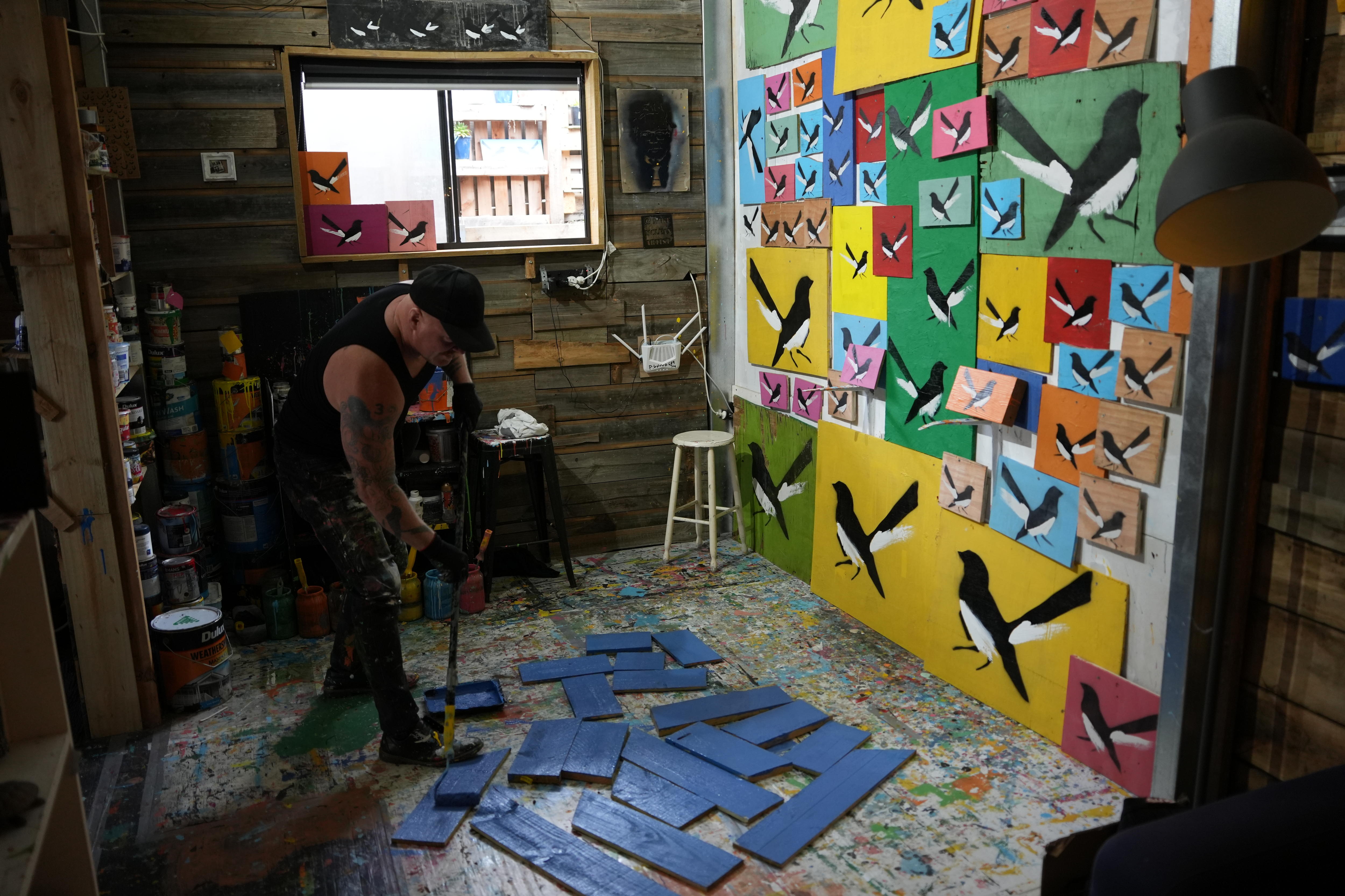Mike Mclean in his Torquay studio using a roller to paint the background of his popular willy wagtails.