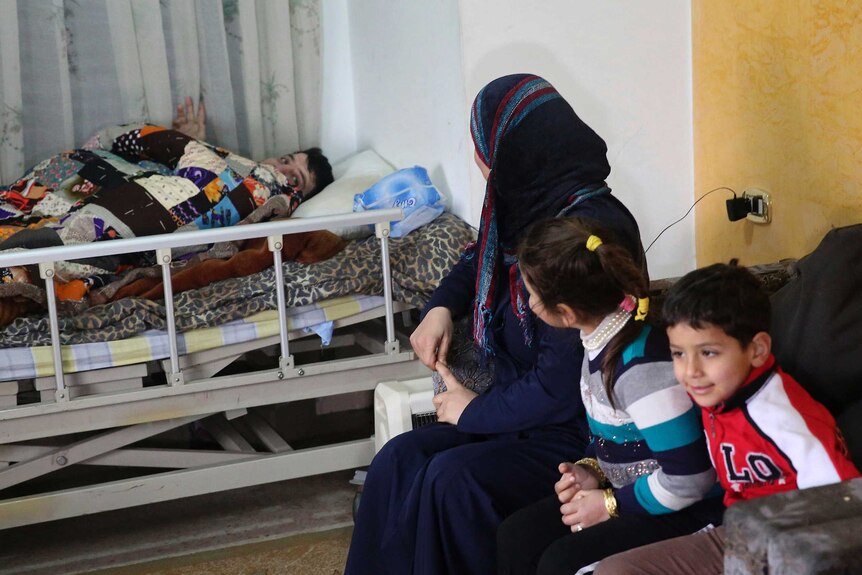 Refugee Nasser Sheik, bedridden after a stroke, talks to his wife Mayada and two children.