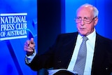 A man in black suit and blue tie points his finger with a blue background behind him and words National Press Club of Australia