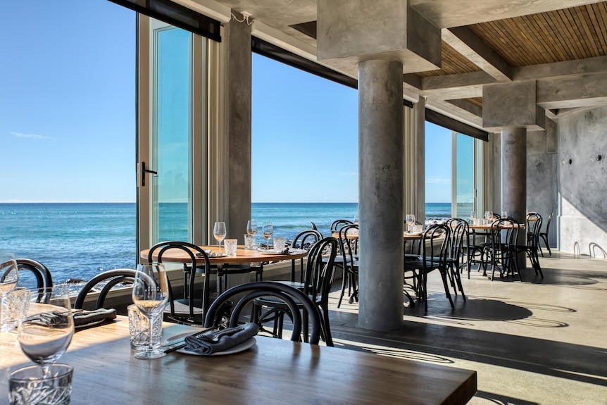 The interior of a modern restaurant, without any customers, with water views out the windows.