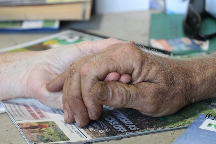 Close up of a man and a woman's hands clasped over a magazine on a table