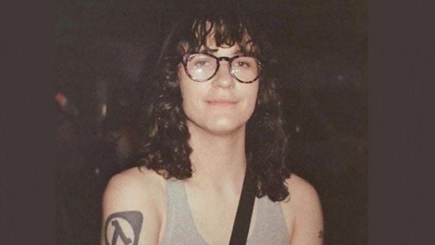 Bridget Flack is pictured with flasses and curly hair and a small smile at the camera