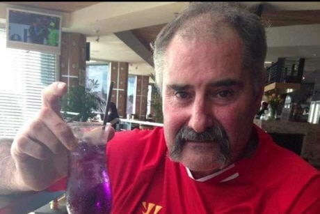 A man in a red soccer shirt holding up a purple cocktail