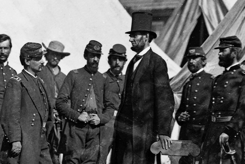 Abraham Lincoln wears a top hat surrounded by a group of officers.