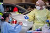 two women in scrubs and PPE holding test tubes surrounded by cars