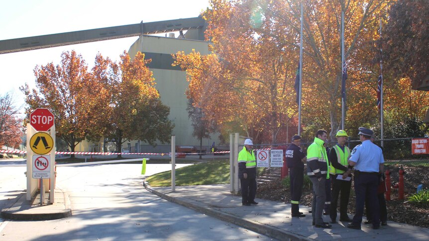 Men in high-vis clothing speak to a police officer in front of the Albury paper mill.