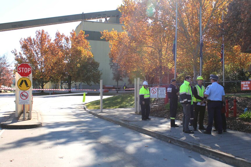 Men in high-vis clothing speak to a police officer in front of the Albury paper mill.