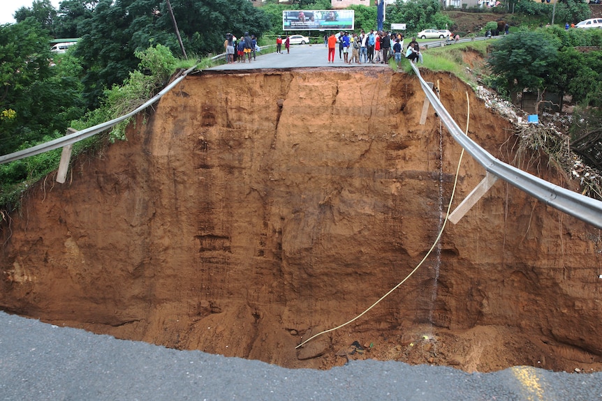 People stand in front of a bridge that was swept away