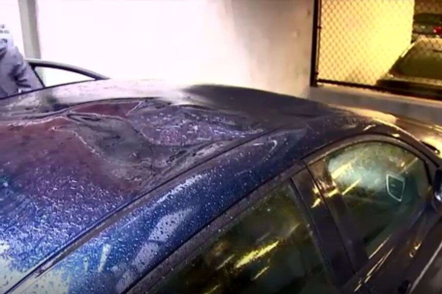 A large dent can be seen on the right side of the roof of a blue sedan