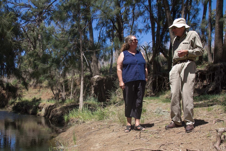 Woman and man standing on riverbank.