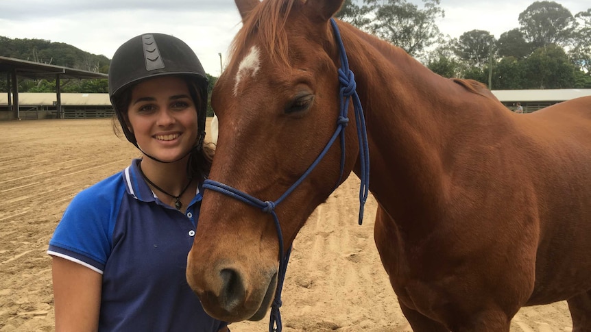 Samantha Monaco stands by a horse that has its eyes closed.