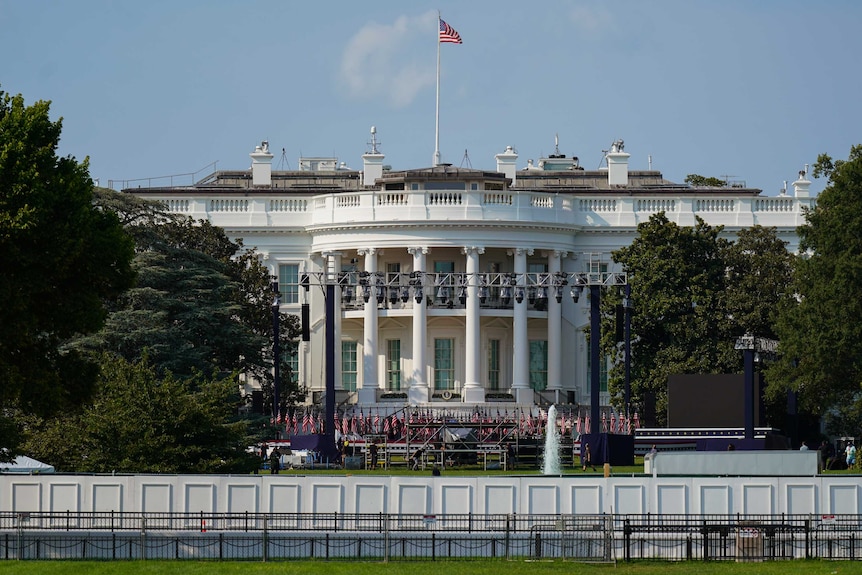 The exterior of the white house with flags and light scaffolding out the front