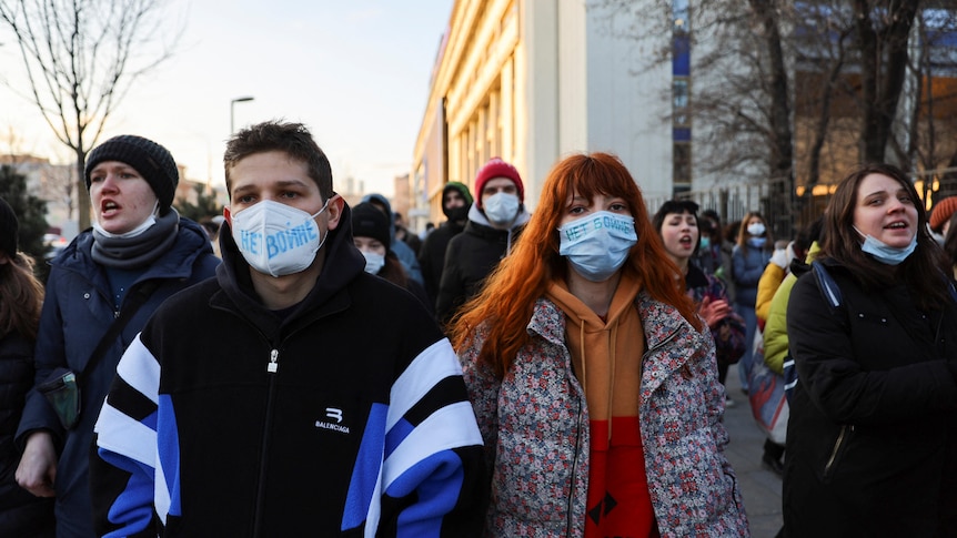 People wearing masks with the slogan "no war" attend a protest