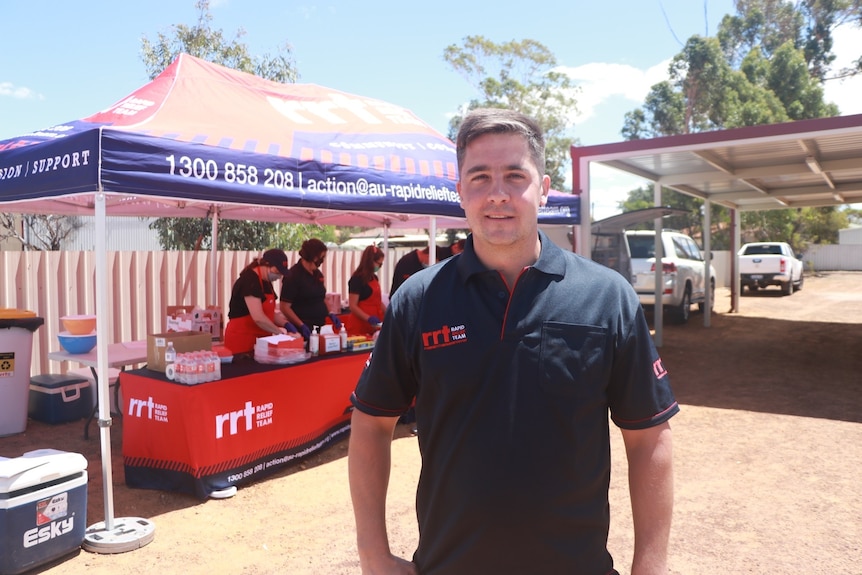 A young man stands in front of a relief tent serving supplies for firefighters.