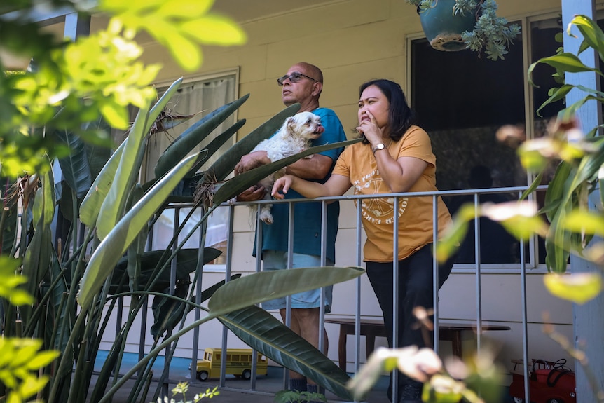 Un hombre sostiene un perro de pie con una mujer en un balcón.