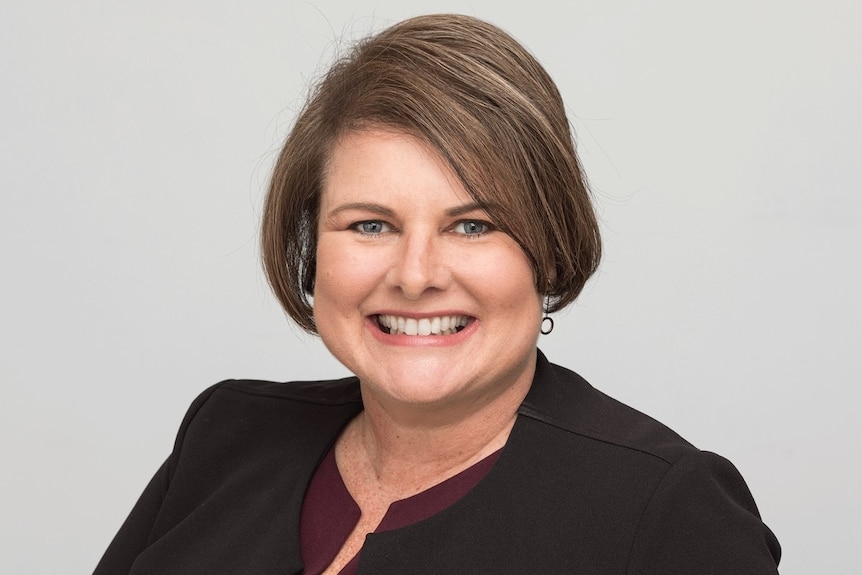 A woman smiles in front of a white background.