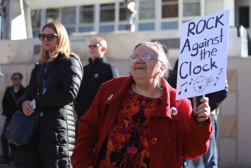 A protester in Canberra waves a sign that says 'rock against the clock'.