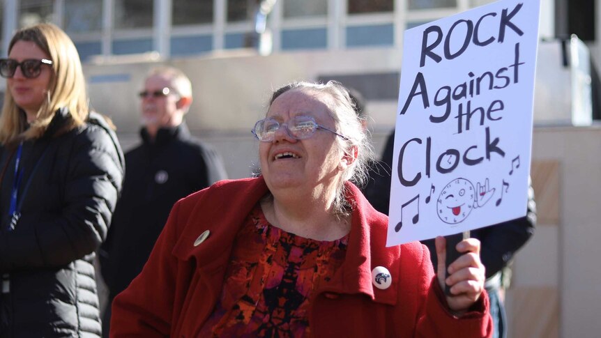 A protester in Canberra waves a sign that says 'rock against the clock'.