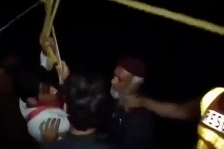 A dark and blurry photo of a boy in a harness being pulled to safety by three men