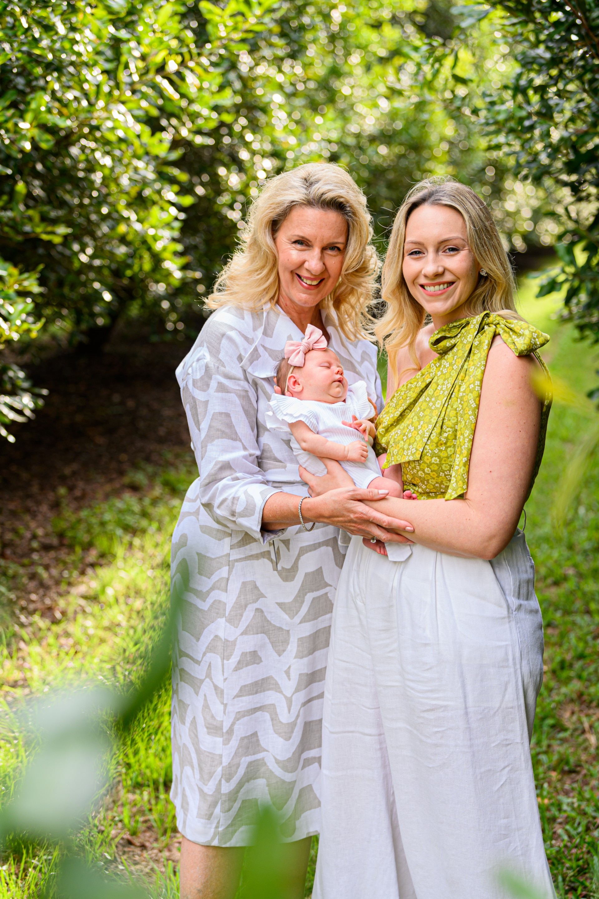 Dos mujeres sostienen a un bebé y sonríen en un huerto de macadamia.