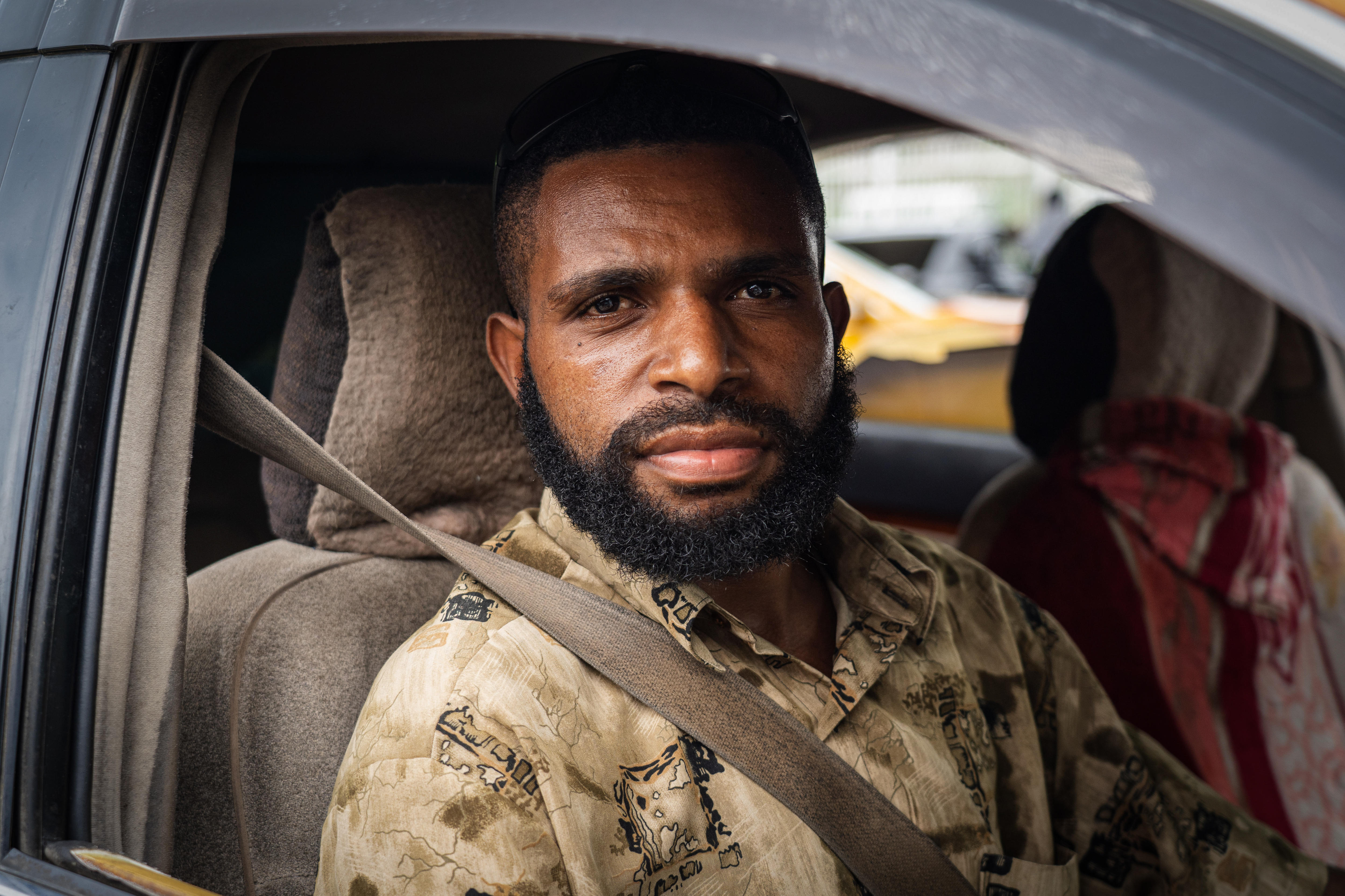 A man looks through the open window of a car, speaking into a microphone