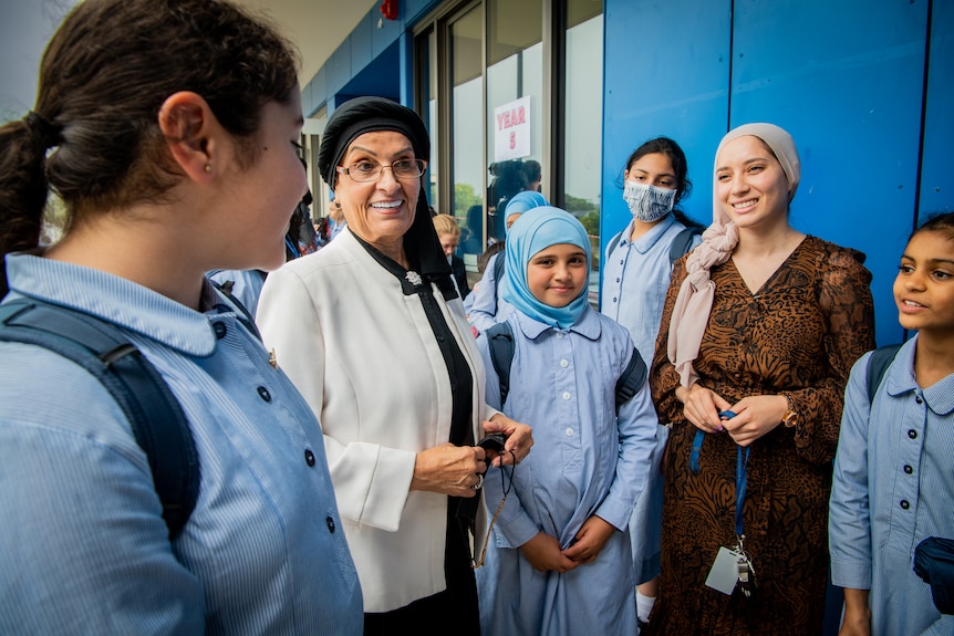 Mona Abdel-Fattah pictured outside at a school, talking with young school students