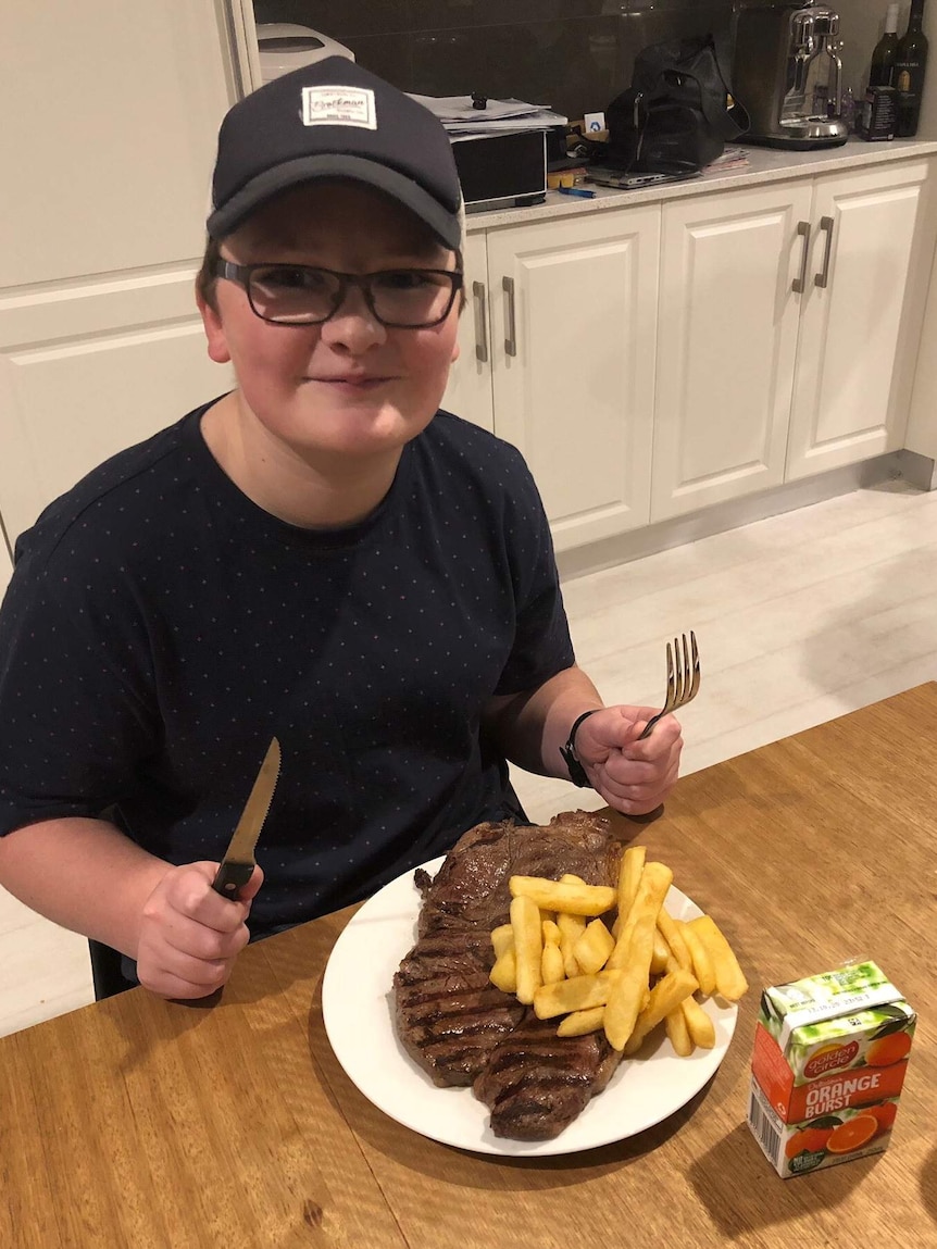 A boy wearing a cap holding a knife and fork