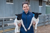 Sophie Curtis stands next to the sheep yards holding two, black-headed lambs on her farm near Millmerran, QLD, in July 2020.