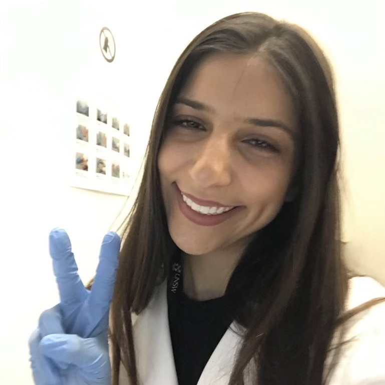 Nita Roschanzamir takes a selfie wearing a white lab coat and a blue glove