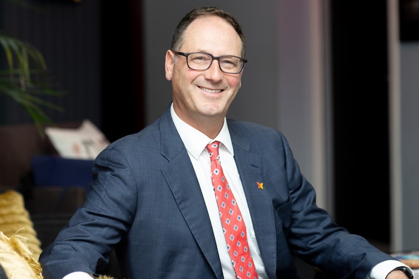 A headshot Dr Grant Blashki, wearing a blue suit and red tie.