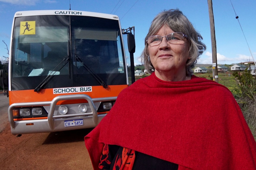 Carolyn Gomersall stands in front of a school bus in a rural setting.