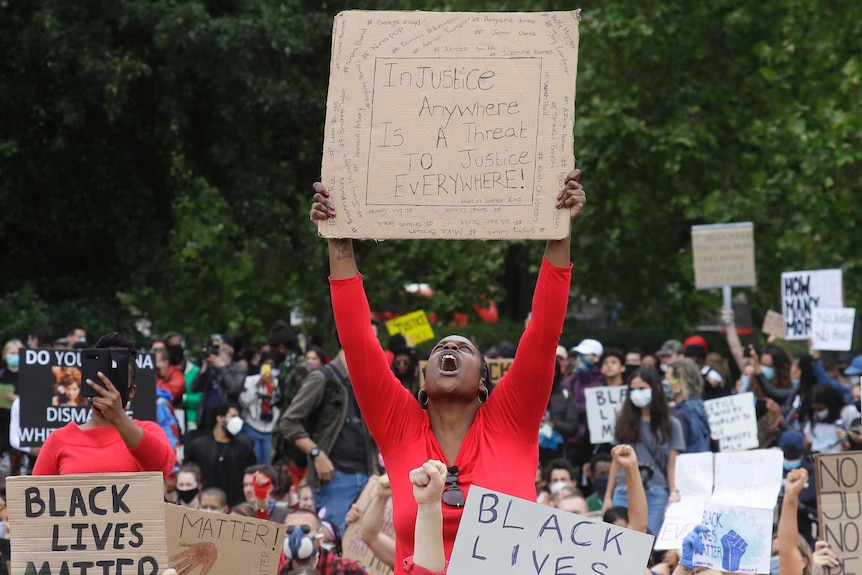 A woman in red screams and holds up a sign about racial injustice.
