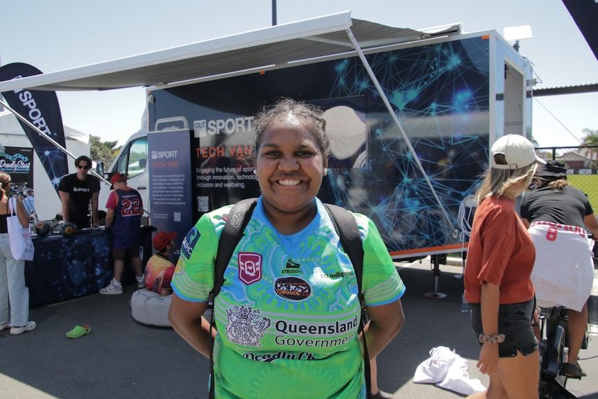 Young Indigenous girl in a rugby jersey smiles warmly at the camera. 