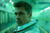 Close-up of Brad Pitt in green-lit space-type hold, wearing space suit but no helmet, looking at camera.