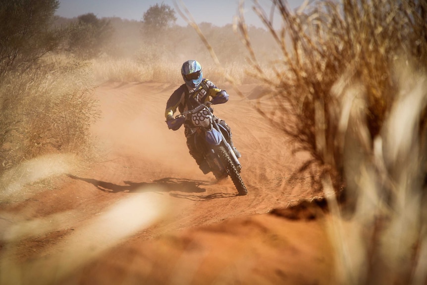 A dirt-bike rider races along a dusty trail.