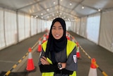 A woman in hi-vis vest stands with her arms crossed in a large tent.