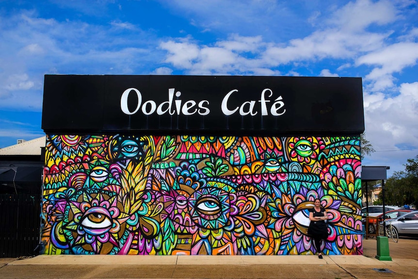 Woman leans against colourful mural on building.