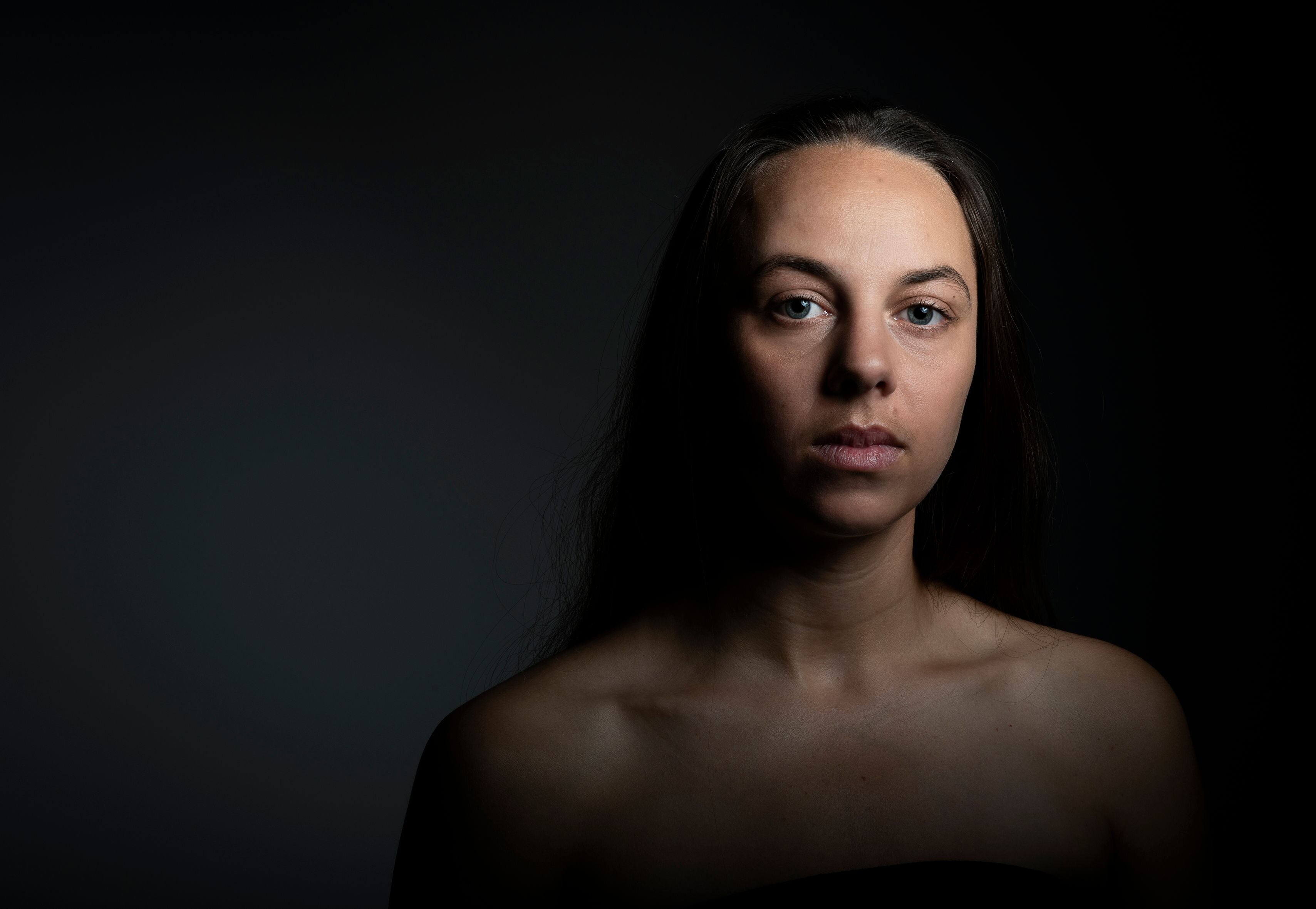 A young woman with long black hair is seriously looking into the camera.