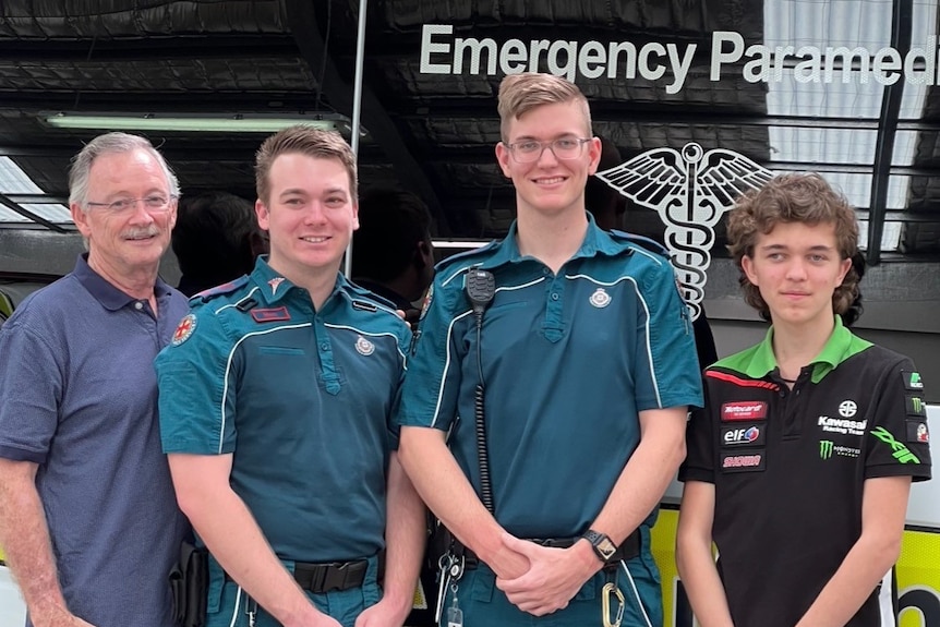A teenage boy with three men, two in paramedic uniforms, in front of an ambulance