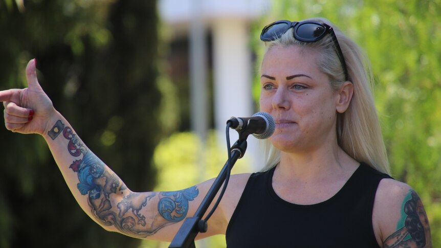 A woman with tattooed arms speaks into a microphone